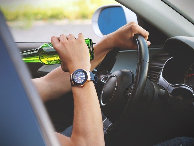 An individual under the age of 18 is drinking a beer and driving a car.