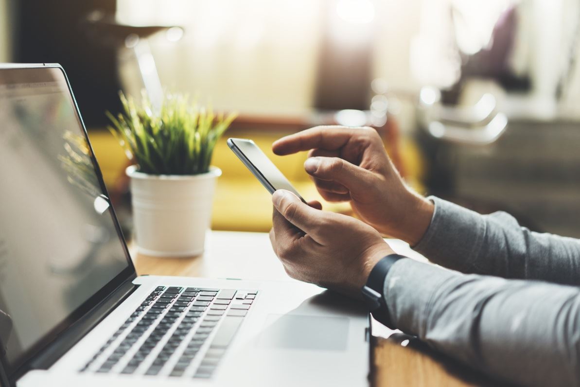 Man using cellphone with open laptop next to him