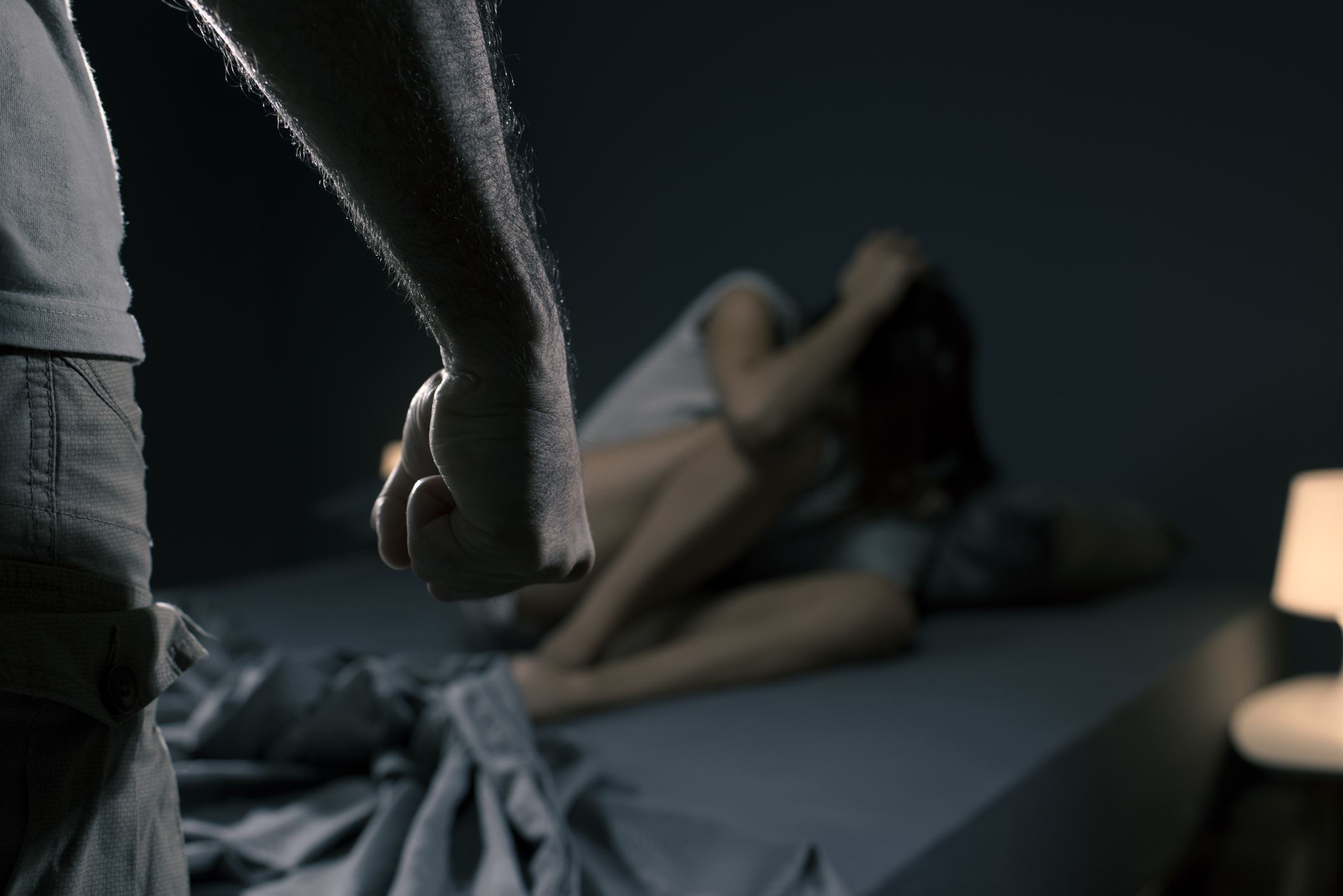man clenching fist while woman sits on bed